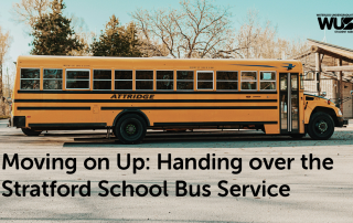 A yellow school bus is parked in a lot surrounded by trees with fall foliage. The text on the image reads, "Moving on Up: Handing over the Stratford School Bus Service." Logos for "WUSA" and "Waterloo Undergraduate Student Association" are at the top right, emphasizing quality school transportation.