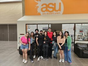 A group of students, alongwith VP Arya smiling, standing outside the 'Arts Student Union' office.