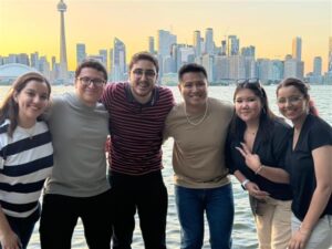 A group of students standing with Arya in front of a scenic skyline background, smiling and posing with arms around each other. 