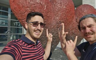 President Nick and VP Arya smiling and pointing to sculptures of red 'hearts' behind them.