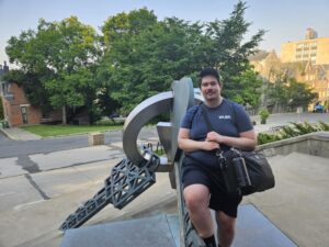 Nick standing in front of a sculpture with a bag. 