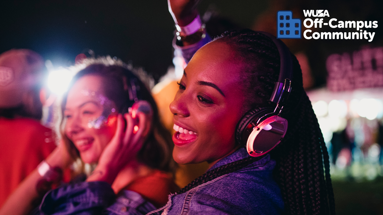 Two people enjoying music at an outdoor event, wearing headphones and smiling, with a vibrant festival atmosphere that feels like a disco after dark.